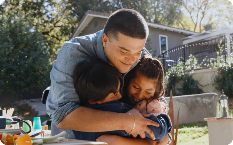 A young man embraces his family members outside of his new home.