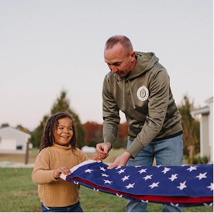 Adult and child smiling as they fold an American flag outside on a sunny day.
